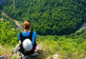 high angle shot of a female hiker sitting at the edge of the cliff looking down at the forest